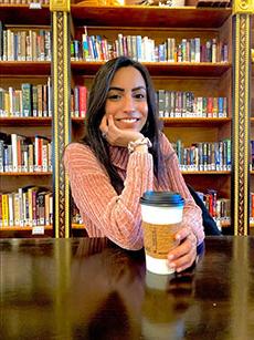 Shabnam Nejat  posing with coffee at a table in front of a wall of books